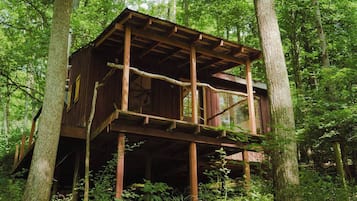 A wooden cabin with a balcony, surrounded by trees.