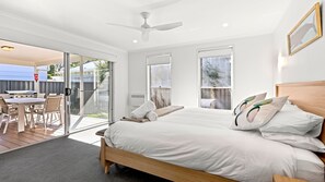 A bedroom with a bed, pillows, a ceiling fan, and a view through a sliding glass door to an outdoor patio area. - Saltwood - Pet Friendly - Community Pool (Callala Beach)