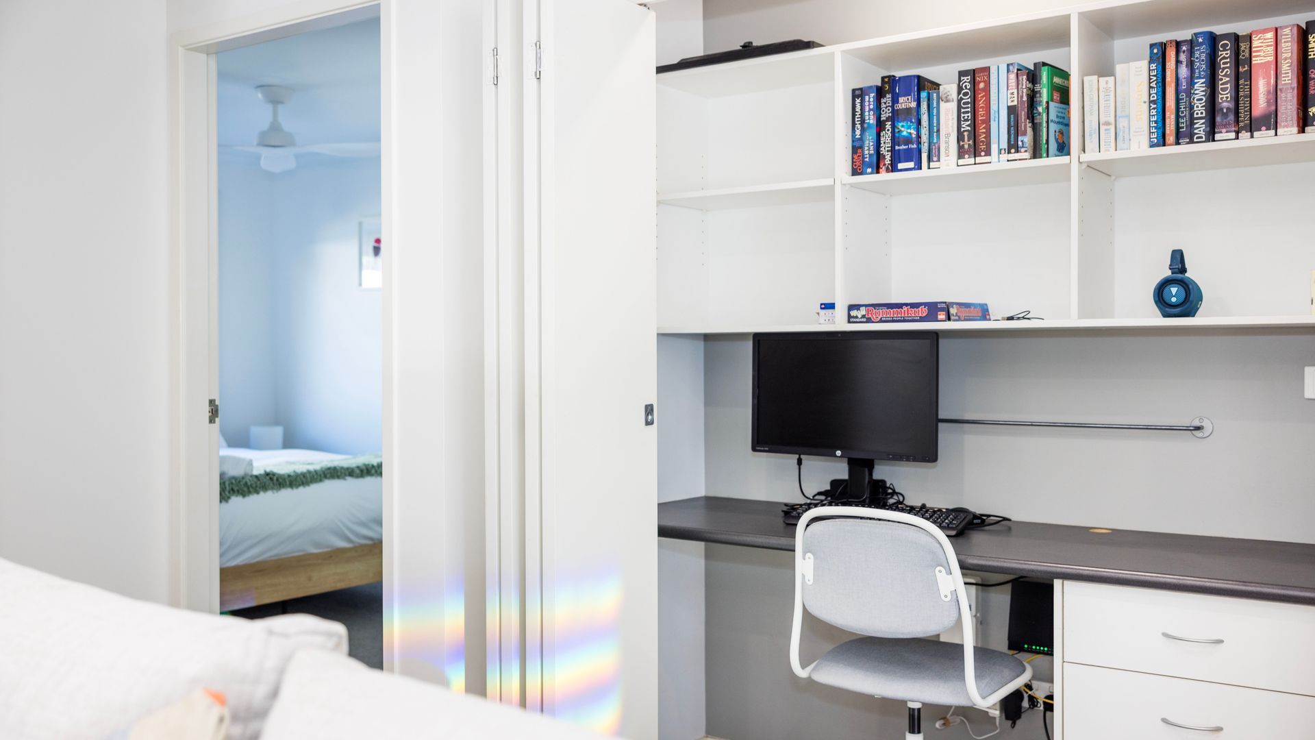 A bedroom with a bed, a desk with a computer, and a bookshelf with books.