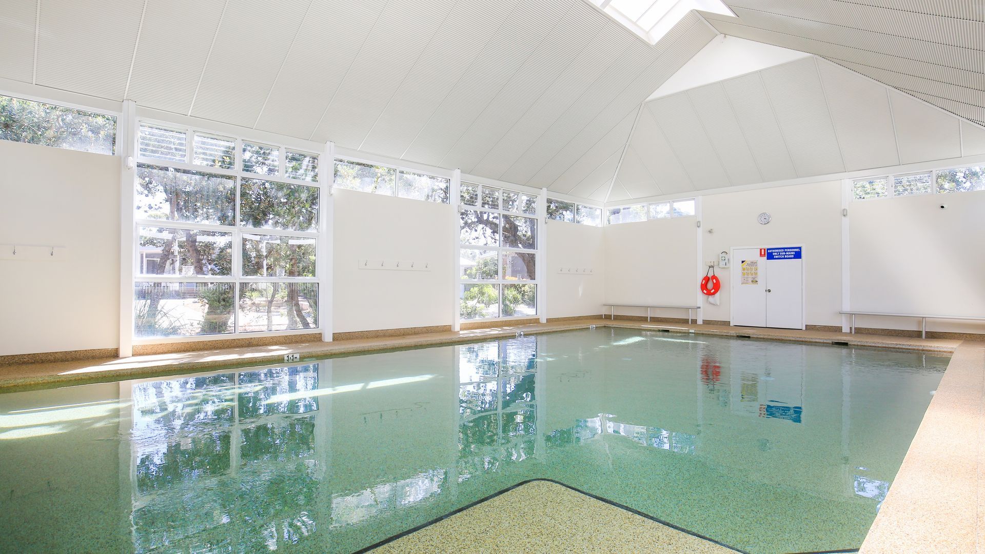 Una piscina interior con paredes de vidrio transparente, piso de baldosas y techo con un diseño geométrico.