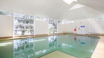 Una piscina interior con paredes de vidrio transparente, piso de baldosas y techo con un diseño geométrico.