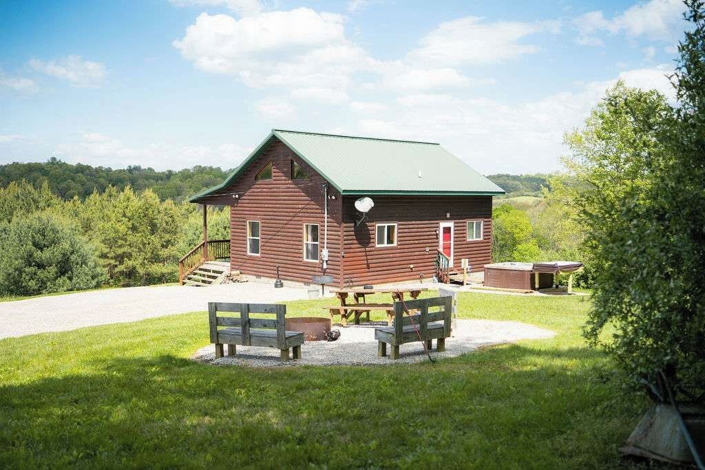 A rustic wooden cabin with a green roof, a porch, and a picnic table with benches.