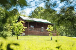 Una cabana amb un porxo, envoltada d'arbres i gespa.