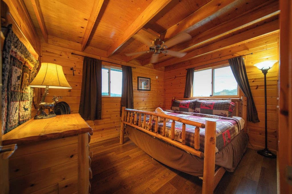 Quarto de cabana de madeira com cama, escrivaninha e ventilador de teto.