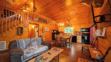 A wooden cabin interior with a sofa, dining table, kitchen, and a staircase.