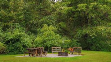 A picnic area with wooden benches and a fire pit surrounded by lush greenery.