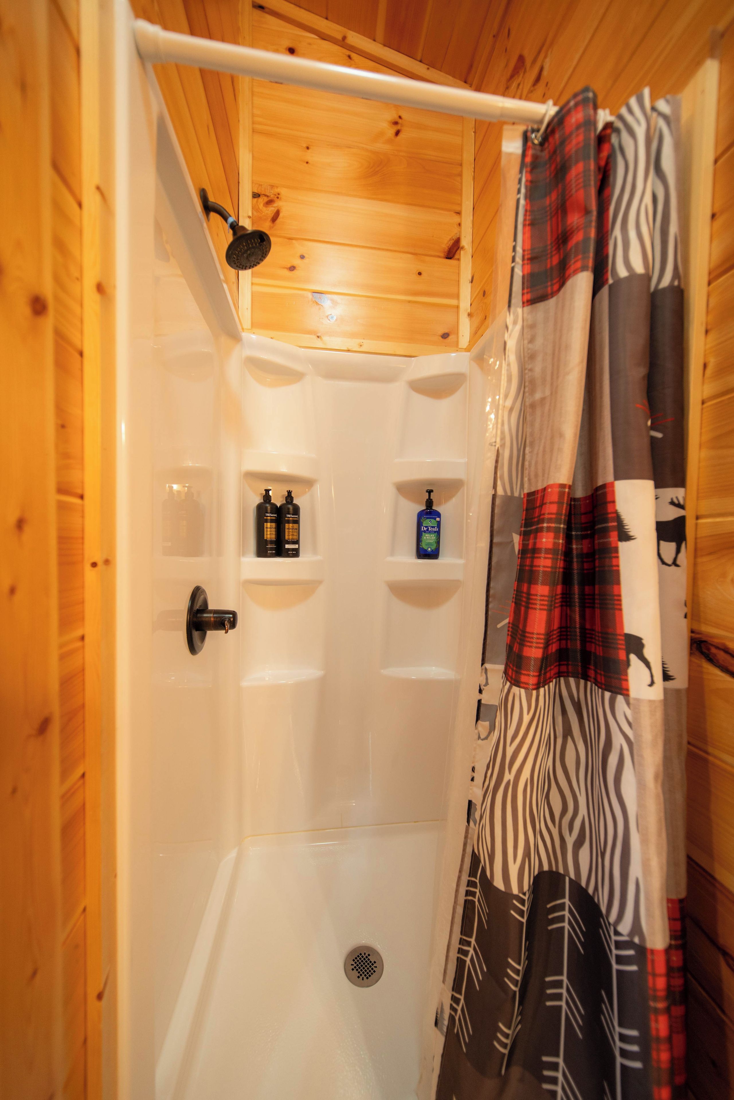 A shower stall with a wooden ceiling, a shower curtain, and a shelf with toiletries.
