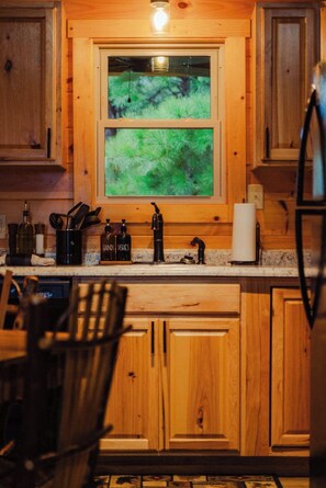 Una cocina con armarios de madera, un ventanal con vista a un paisaje verde y diversos utensilios de cocina sobre la encimera.