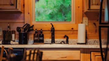 A kitchen with wooden cabinets, a double sink, and a window with a view of greenery.