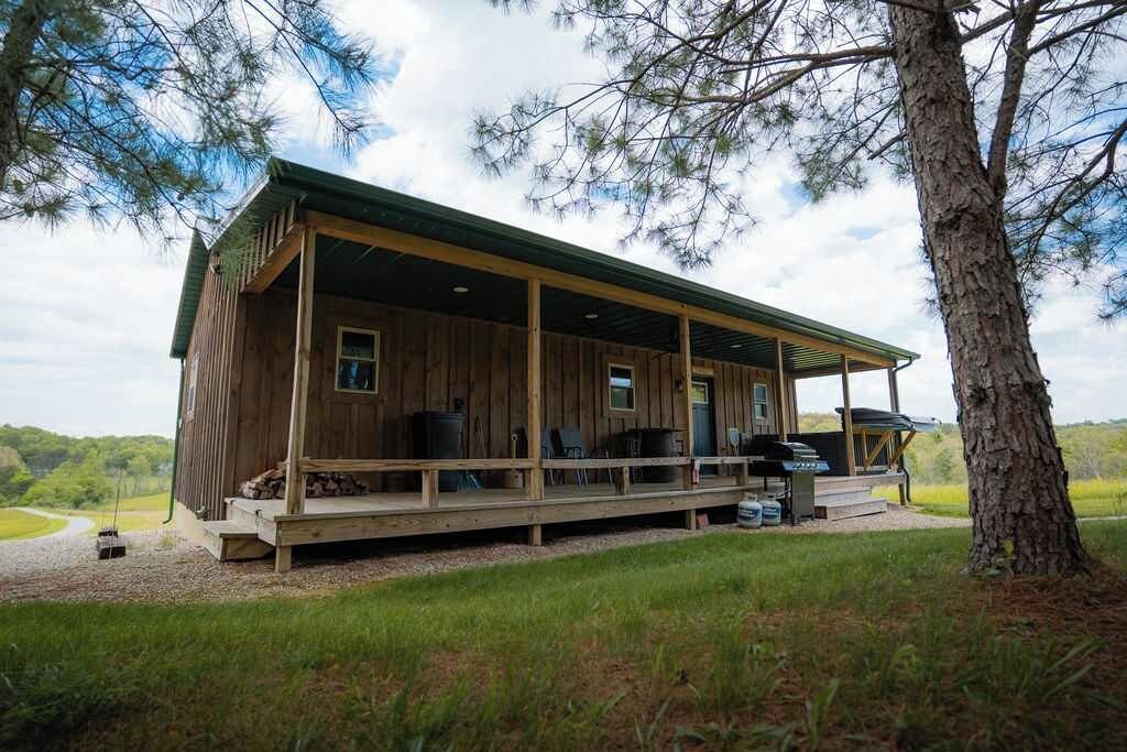 A wooden cabin with a covered porch, outdoor seating, and a grill area.