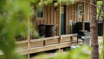A wooden cabin with a deck, a barbecue grill, and outdoor seating.