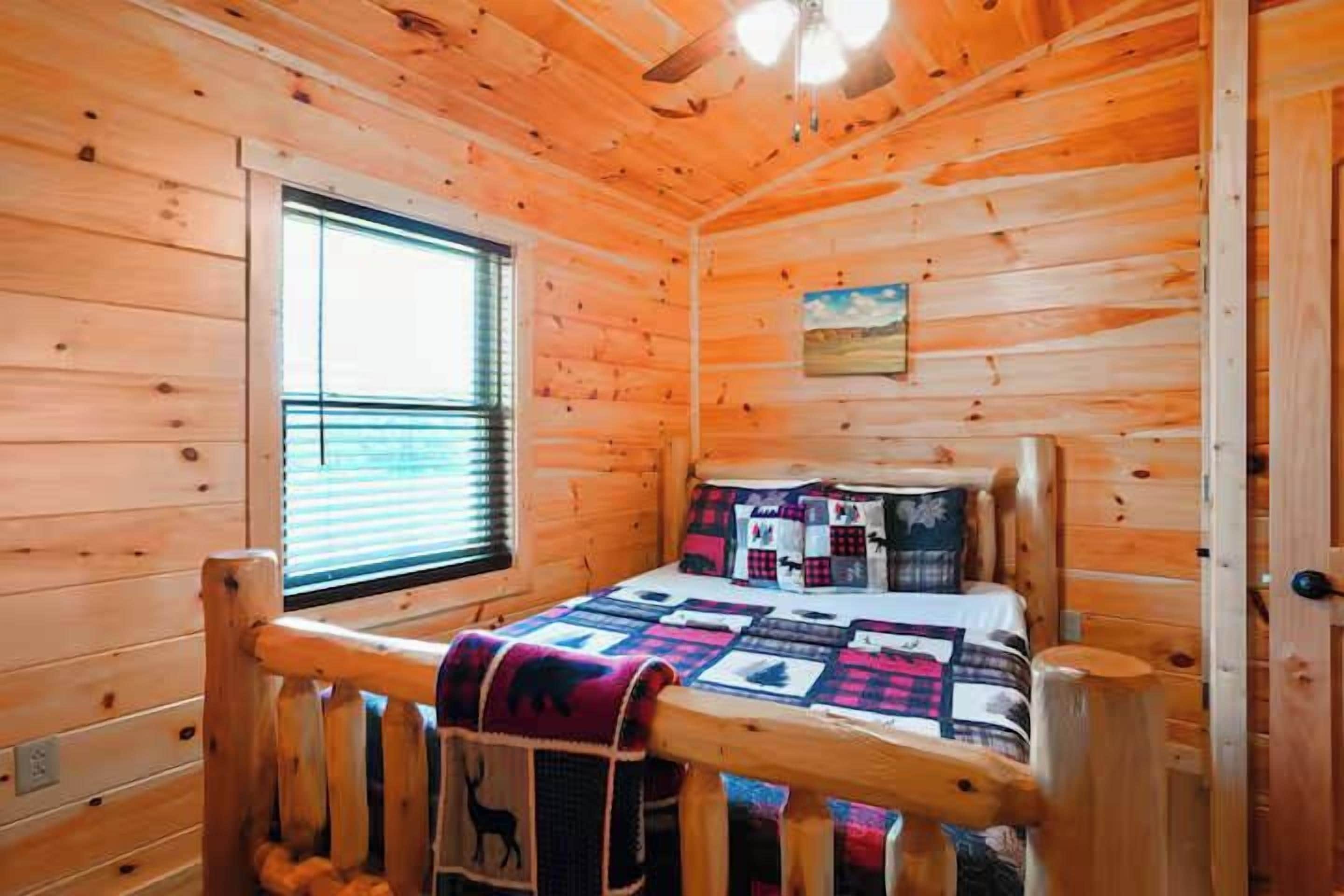 Habitación de cabaña de madera con cama, ventana y ventilador de techo.