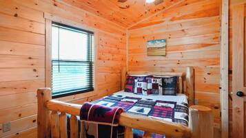 Habitación de cabaña de madera con cama, ventana y ventilador de techo.