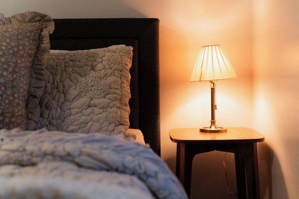 A bed with a textured blanket, a pillow with a ruffled edge, and a bedside table with a lamp.