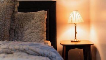 A bed with a textured blanket, a pillow with a ruffled edge, and a bedside table with a lamp.
