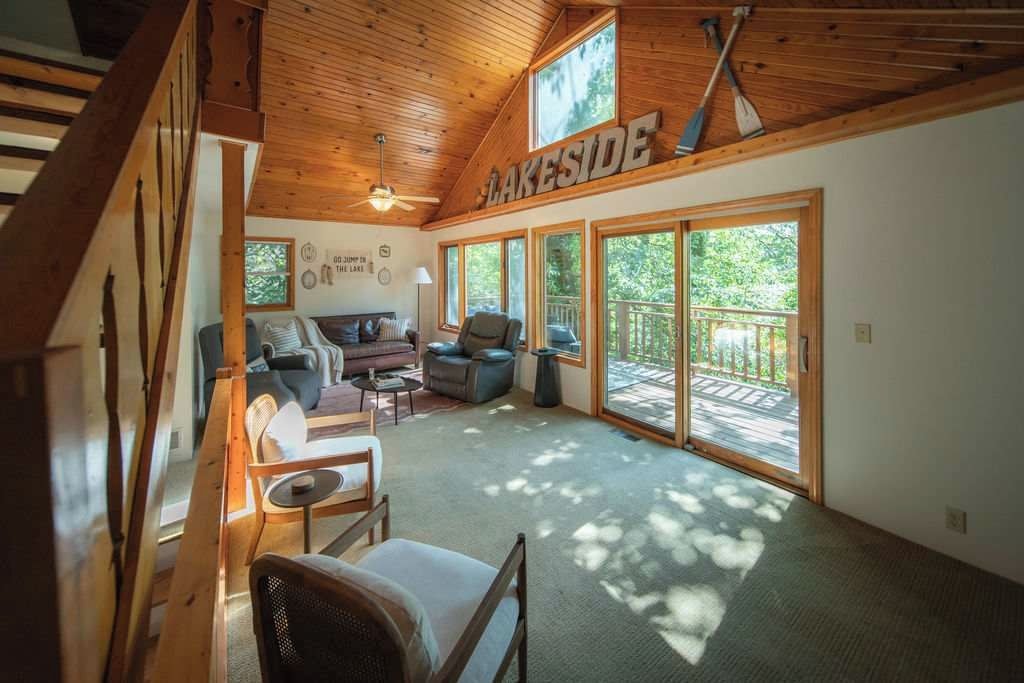 Amplia habitación con un gran ventanal corredero que da a una terraza, techo de madera y un cartel que dice 'LAKESIDE'.