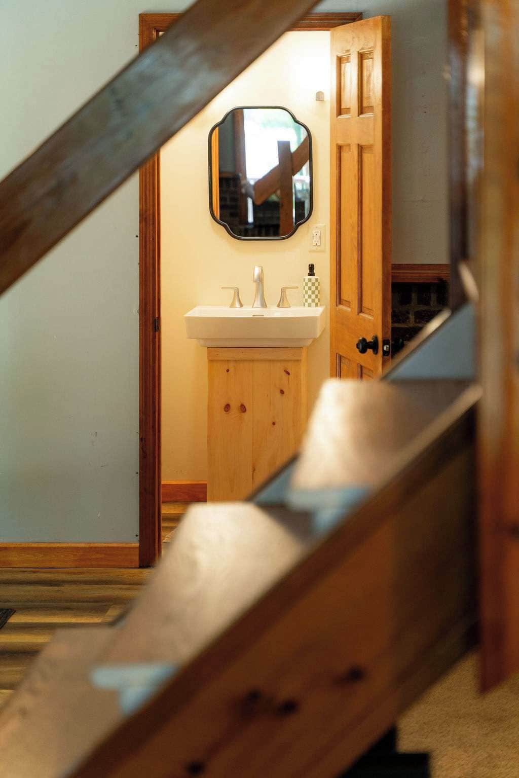 Una escalera de madera que lleva a un baño con un lavamanos blanco y un espejo encima.