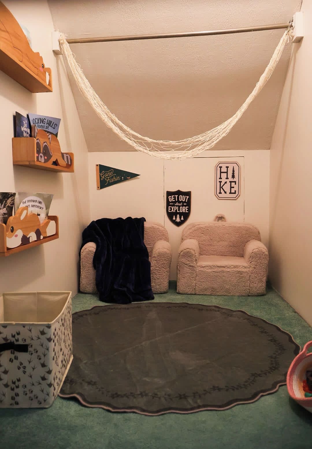Una habitación acogedora con una hamaca, dos sillones mullidos, un tapete pequeño y decoraciones en la pared que incluyen un cartel con la inscripción 'Get Out and Explore' y un cartel con la palabra 'Hike'.