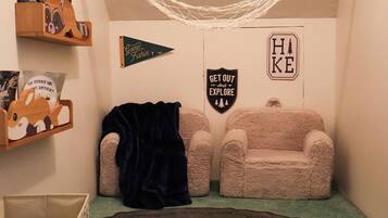 Una habitación acogedora con una hamaca, dos sillones mullidos, un tapete pequeño y decoraciones en la pared que incluyen un cartel con la inscripción 'Get Out and Explore' y un cartel con la palabra 'Hike'.