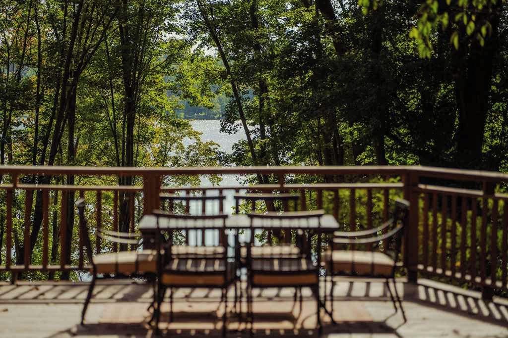 A deck with chairs and tables overlooking a body of water, surrounded by trees.