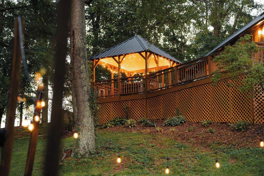 A wooden gazebo with a metal roof, surrounded by a wooden deck and a lattice fence.
