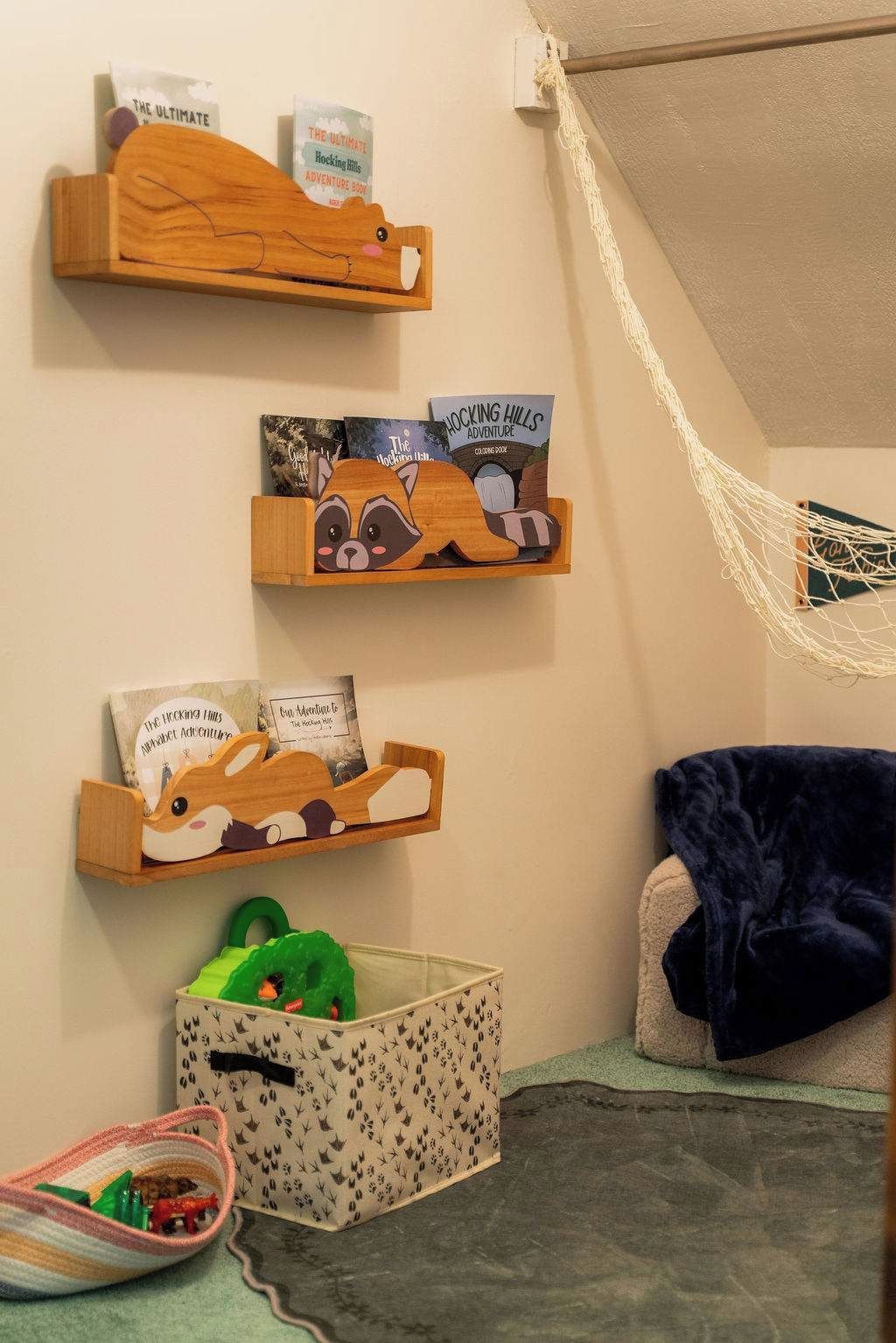 A room with three wooden shelves holding books and a small storage box with toys.