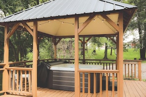 Um gazebo de madeira com hidromassagem, cercado por um deck e árvores.