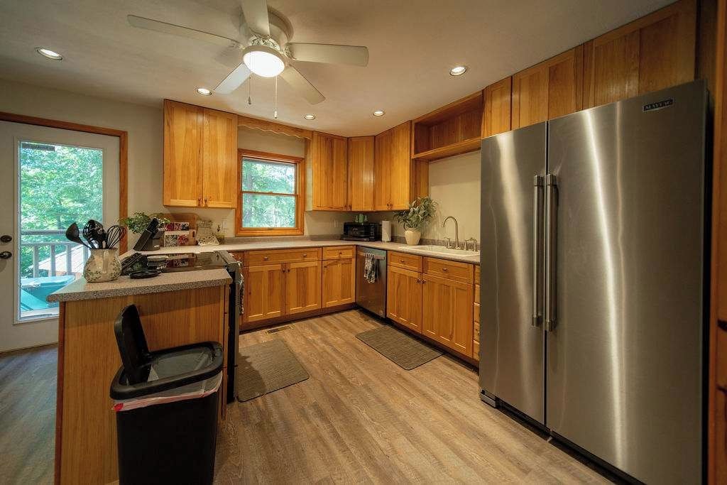 A kitchen with wooden cabinets, a stainless steel refrigerator, a ceiling fan, and a window providing natural light.