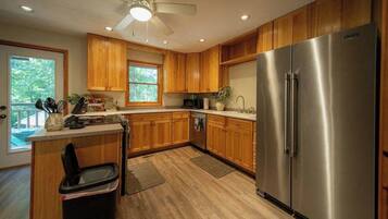 A kitchen with wooden cabinets, a stainless steel refrigerator, a ceiling fan, and a window providing natural light.