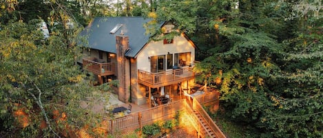 A two-story cabin with a balcony, surrounded by dense forest.