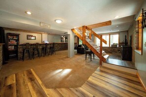 A spacious room with a wooden staircase, a bar area, and a fireplace. - Waterfront Lake Views Villa With Hot tub in Hocking Hills (Logan)