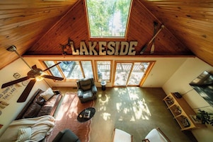 Interior acogedor de una cabaña con un ventanal grande, un ventilador de techo y un letrero que dice 'LAKESIDF'.