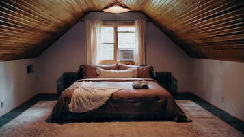 Un dormitorio con techo inclinado, una cama con colcha escocesa, una ventana con cortinas y una lámpara colgante.