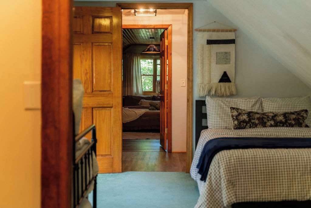 Un dormitorio con una colcha a cuadros, una puerta de madera que da a un pasillo y un tapiz colgado en la pared.