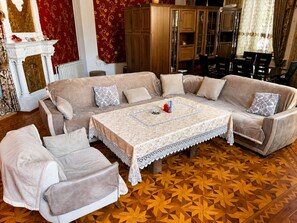 Ein Zimmer mit einem großen beigefarbenen Sofa, einem passenden Sessel, einem mit Spitze bedeckten Couchtisch und einem Holzboden mit Muster.