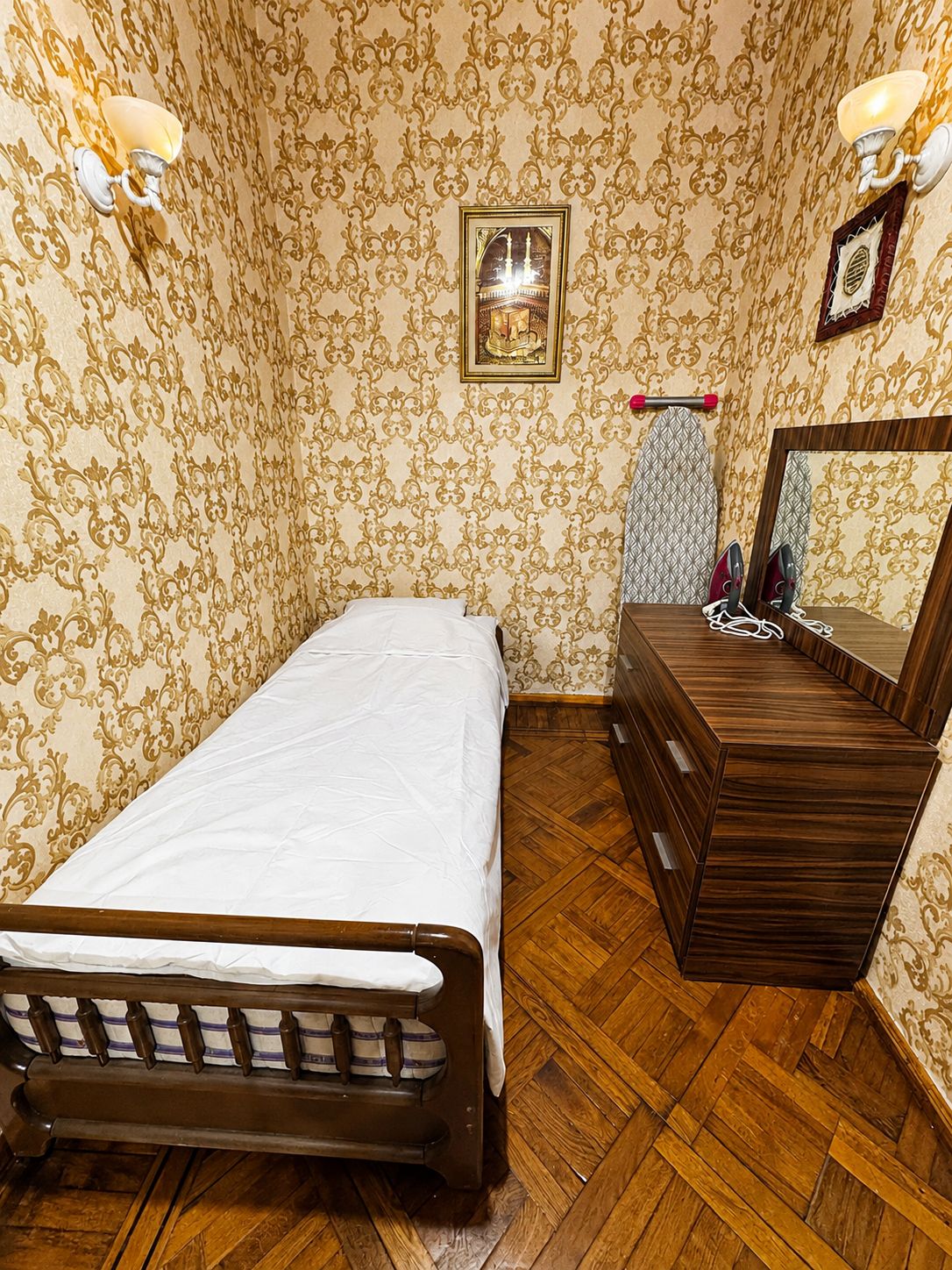 Une chambre à coucher avec un lit en bois, une commode, un miroir et un papier peint à motifs.