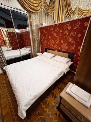 A hotel room with a large bed, a wooden headboard, a mirror, and a wooden floor with a geometric pattern. - Prime Bulbul Avenue Cozy Stay near Nizami & Sea (Bakı)