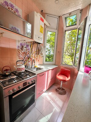 Une cuisine avec des meubles de couleur rose, un four Bosch, une cuisinière à gaz et une chaise rouge.