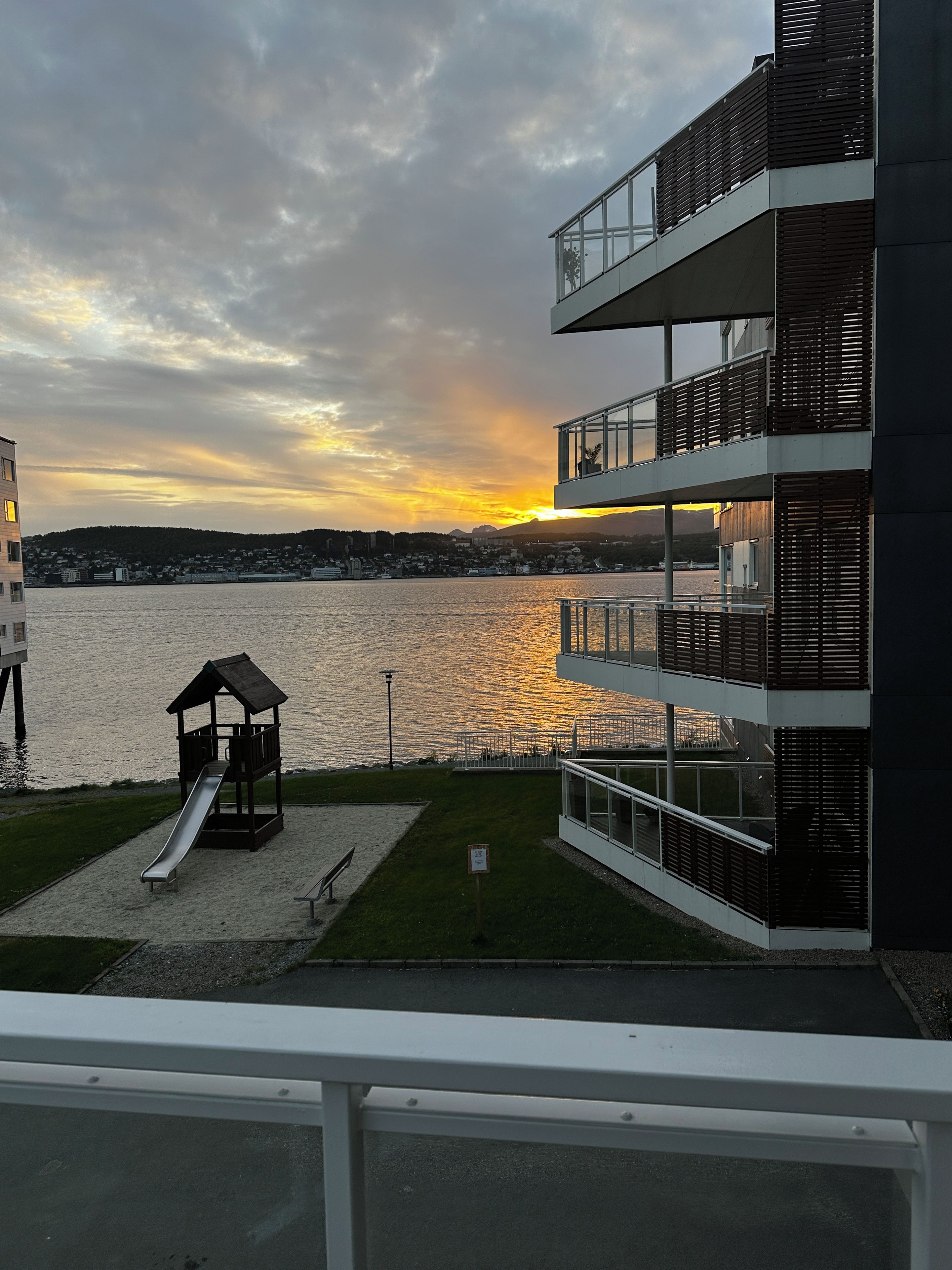 Vista al agua con un parque infantil y un edificio moderno con balcones.