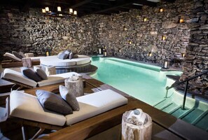 A spa area with stone walls, a pool, and lounge chairs.