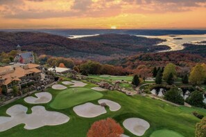 A golf course with bunkers, a clubhouse, and a scenic view of a lake and forest.