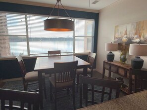 A dining area with a table and chairs, a hanging light fixture, and a view of the water through large windows. - Sunset Shores: Waterfront Views + Pool, Branson & Golf Access (Hollister)