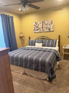 A bedroom with a bed, curtains, a lamp, and a ceiling fan.