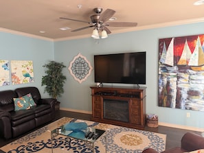 A living room with a ceiling fan, a flat-screen TV, a fireplace, and artwork on the walls.