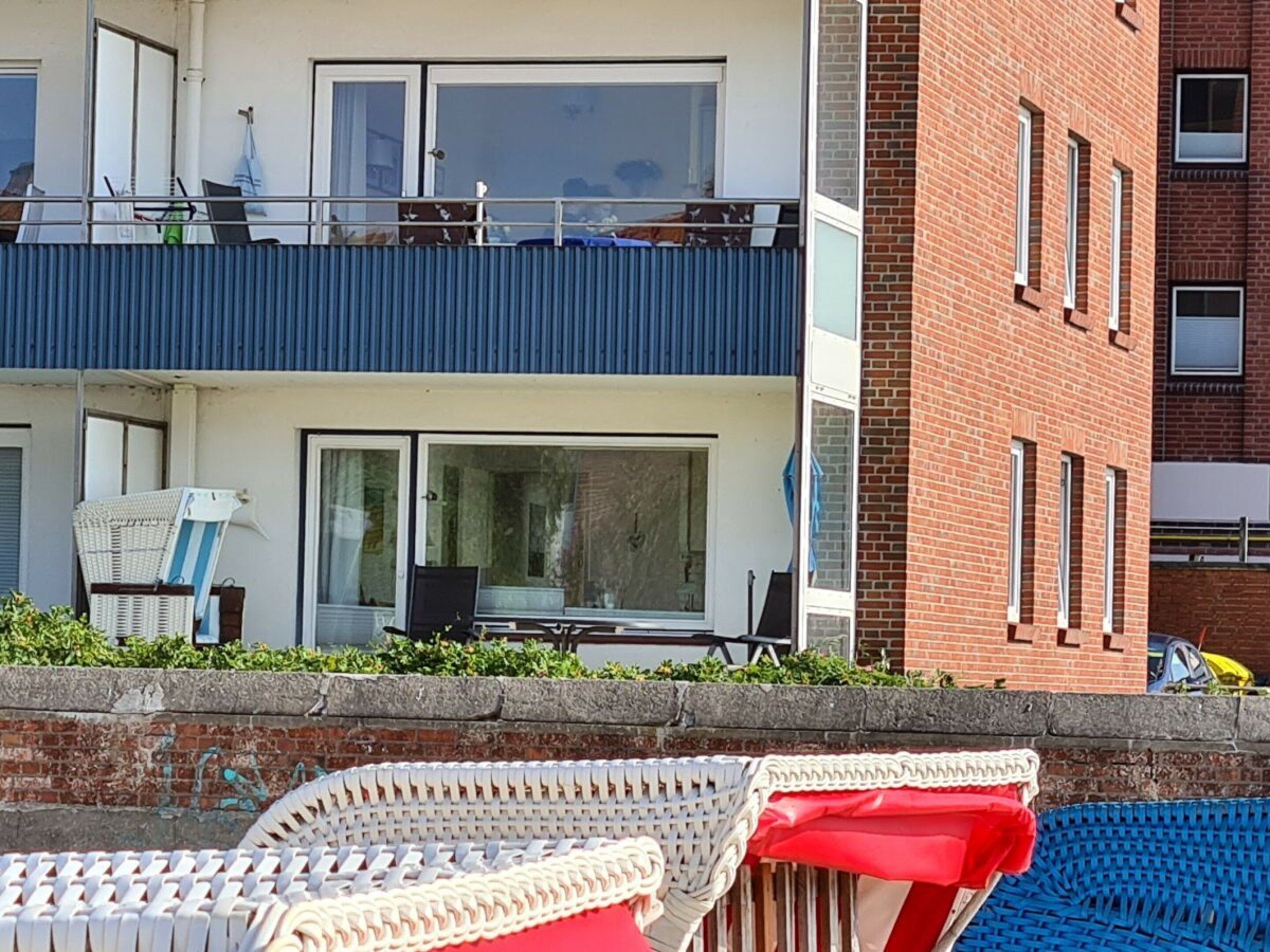 A two-story building with a balcony, a dining area with a table and chairs, and a brick wall.
