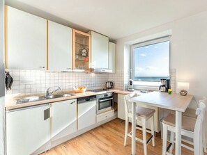 A modern kitchen with white cabinets, a wooden countertop, and a view of the sea through a large window. - 5 - Konigstrasse 5 (Wyk auf Foehr)