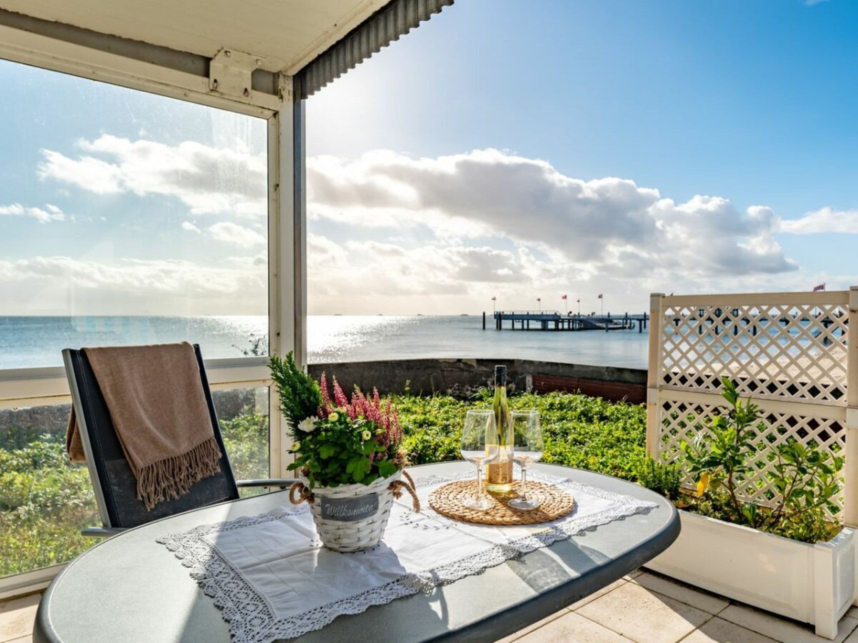 Ein Balkon mit Tisch für zwei Personen, mit Blick auf einen Strand und einen Steg.