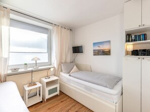 A compact room with a bed, a bedside table with a lamp, a TV mounted on the wall, and a bookshelf. - 5 - Konigstrasse 5 (Wyk auf Foehr)