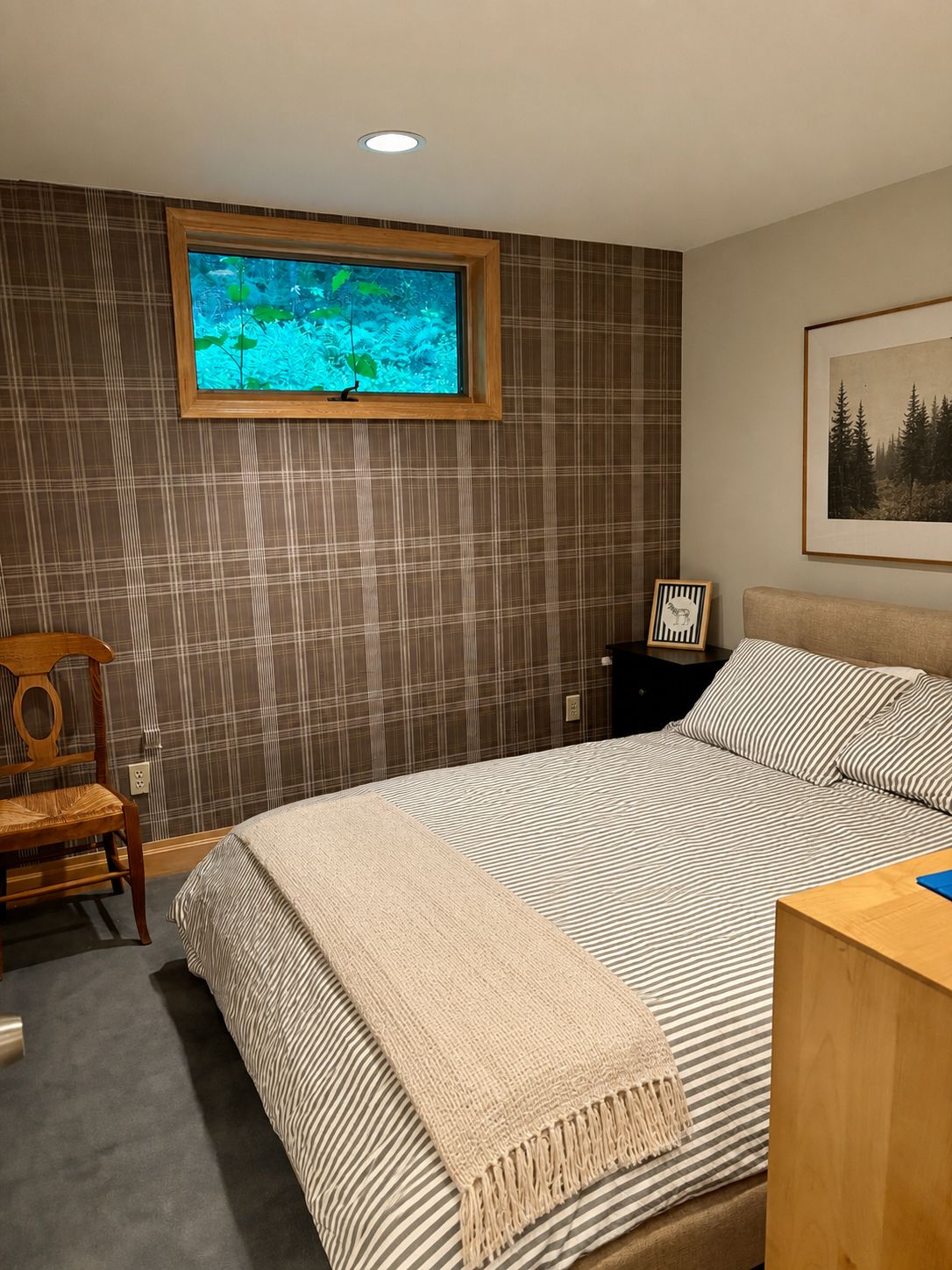 Een slaapkamer met een bed, een raam met uitzicht op water, een lijst met een afbeelding aan de muur en een houten nachtkastje.