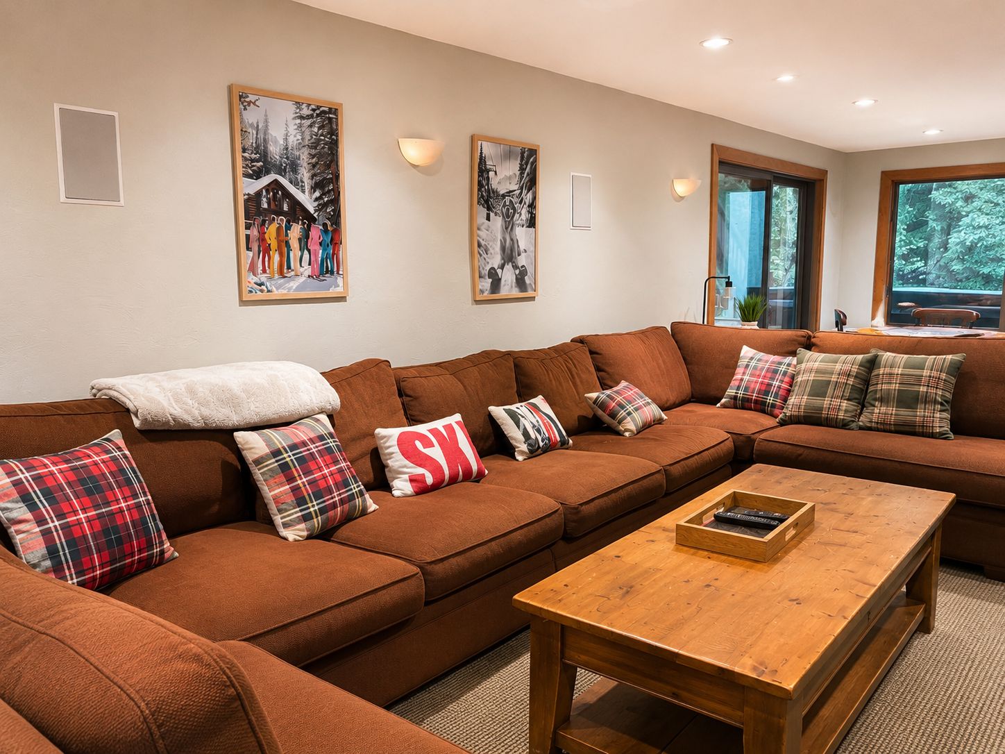 Ein gemütliches Wohnzimmer mit einem braunen Ecksofa, karierten Kissen und einem Holztisch.